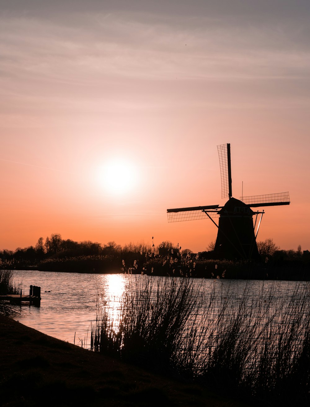 silhouette of windmill near body of water during sunset