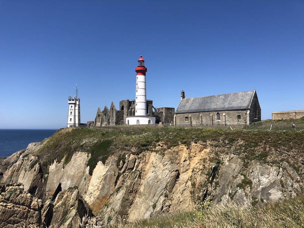 white and red lighthouse on brown and green mountain under blue sky during daytime