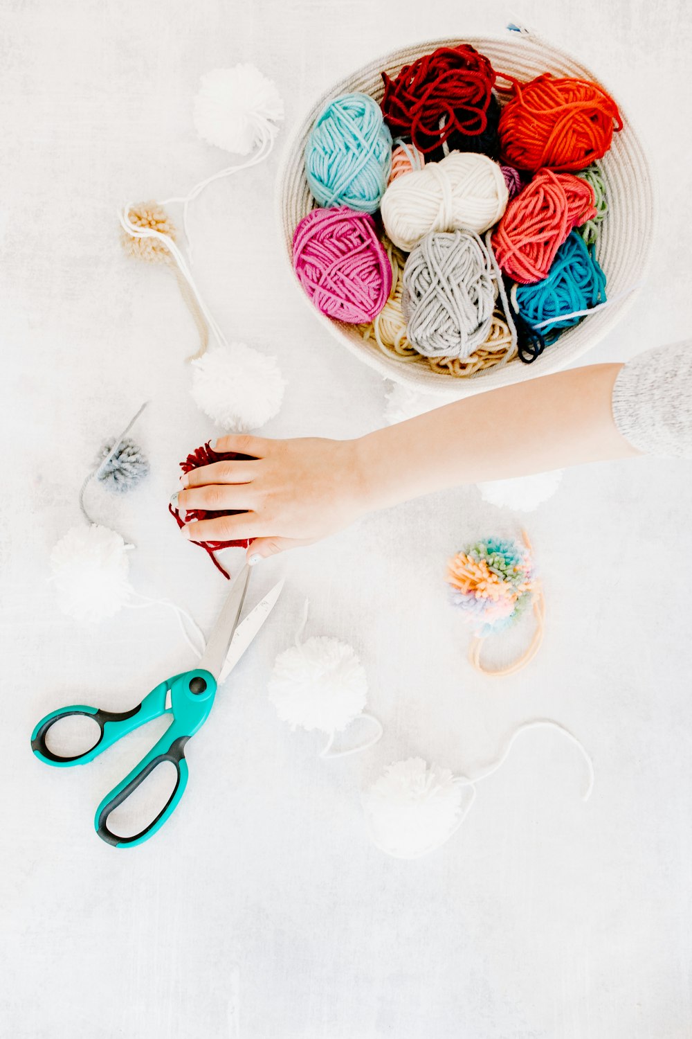 person holding red scissors and white yarn