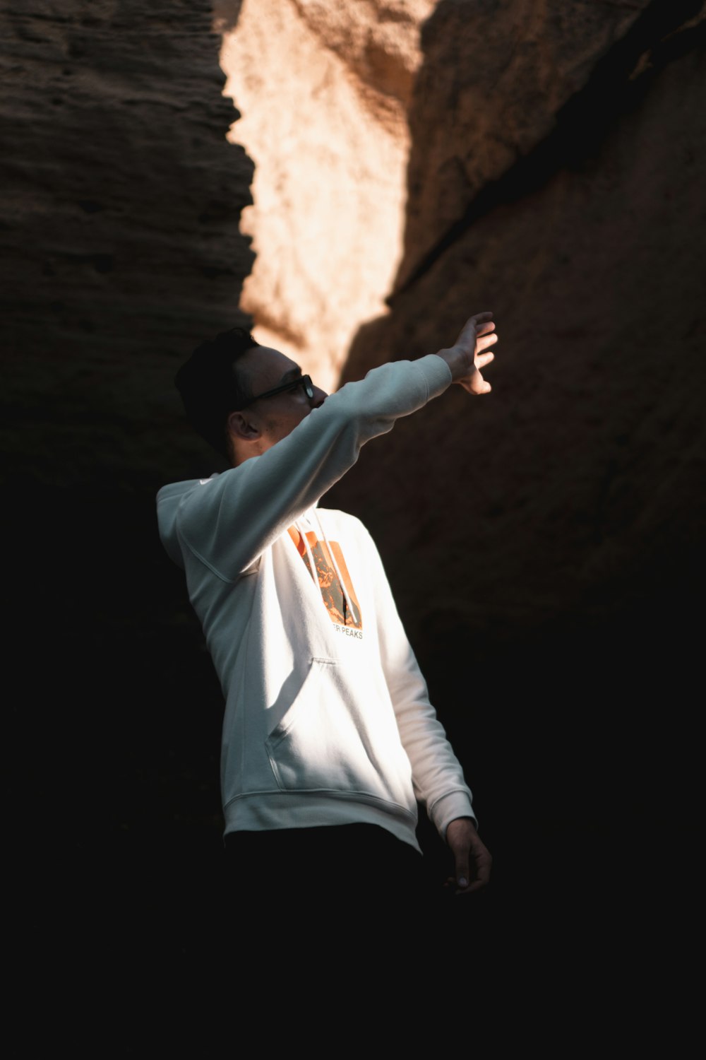 man in white hoodie standing in front of brown rock formation during daytime