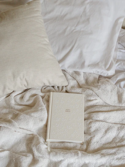 A serene off-white devotional book with a beige textured fabric cover lying on a soft linen cloth.