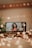 A smartphone displays a video call with a woman holding a guitar, smiling warmly against a softly blurred background. The scene is illuminated by warm, bokeh fairy lights, adding a cozy, intimate atmosphere. Nearby, a book titled 'Fifty Shades Darker' is partially visible, enhancing the setting.