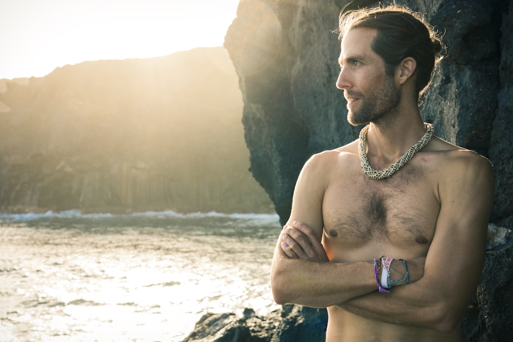 Hombre en topless con collar de plata de pie en la playa durante el día