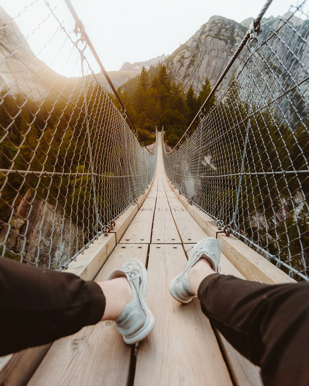 person in white sneakers standing on hanging bridge