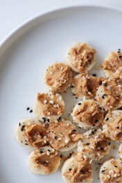Slices of banana topped with peanut butter and sprinkled with black and white sesame seeds on a white plate.