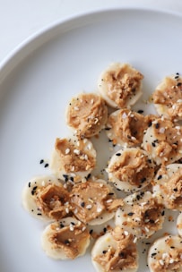 Slices of banana topped with peanut butter and sprinkled with black and white sesame seeds on a white plate.