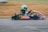 A person wearing a green helmet and black race suit drives a go-kart on a racetrack. The go-kart is blue with red and white accents, featuring the number 107 prominently. The background is blurred, indicating motion and speed.