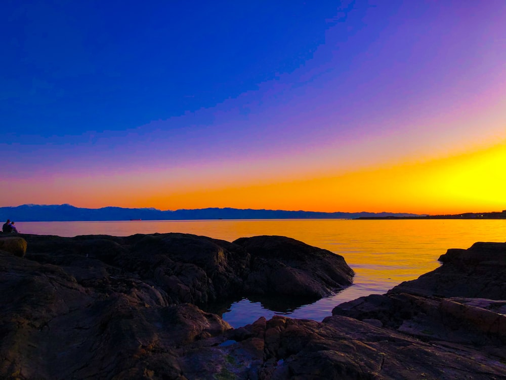 black rock formation near body of water during sunset