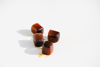 Four small, brown ice cubes are positioned on a white surface, casting faint shadows.