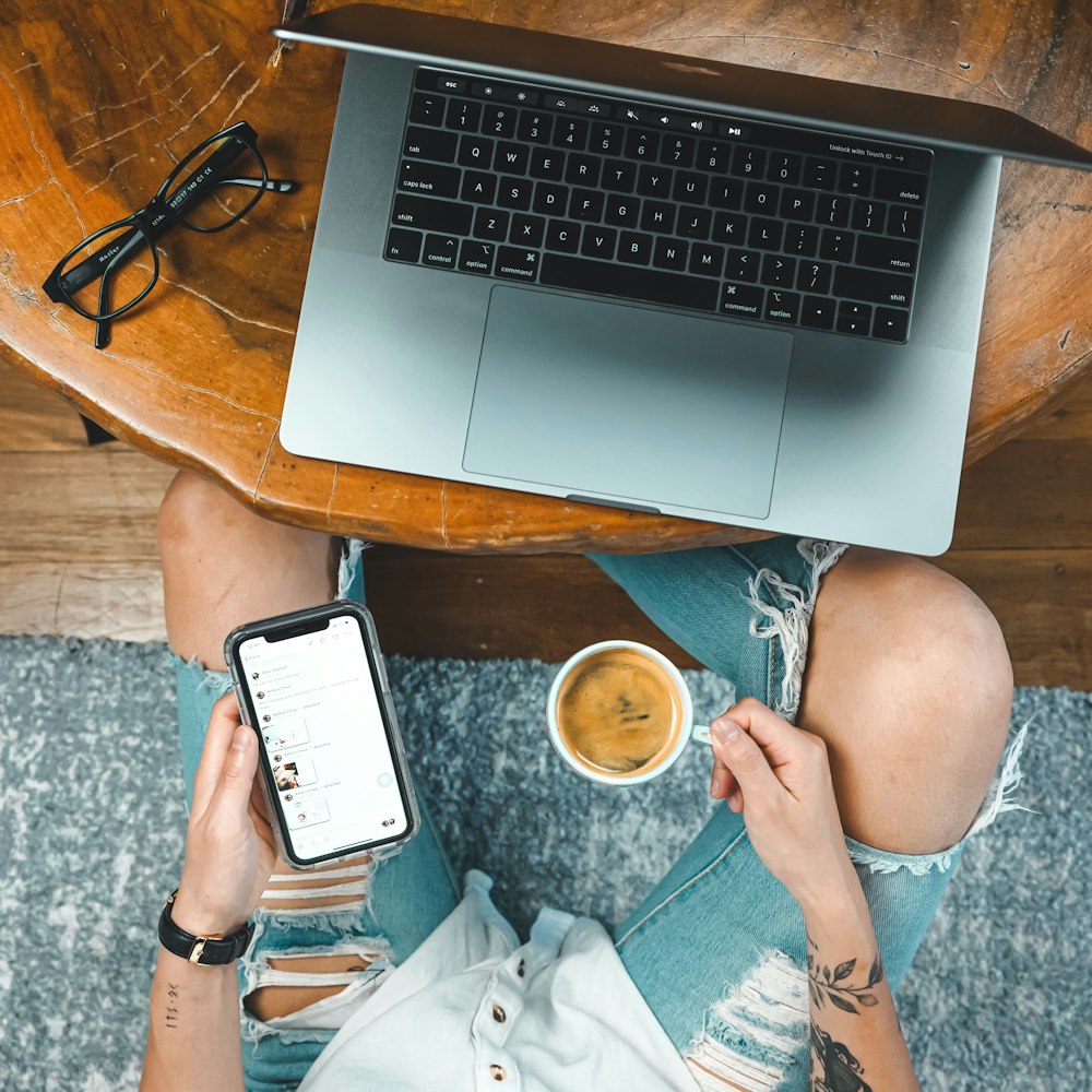 person holding black smartphone near macbook pro