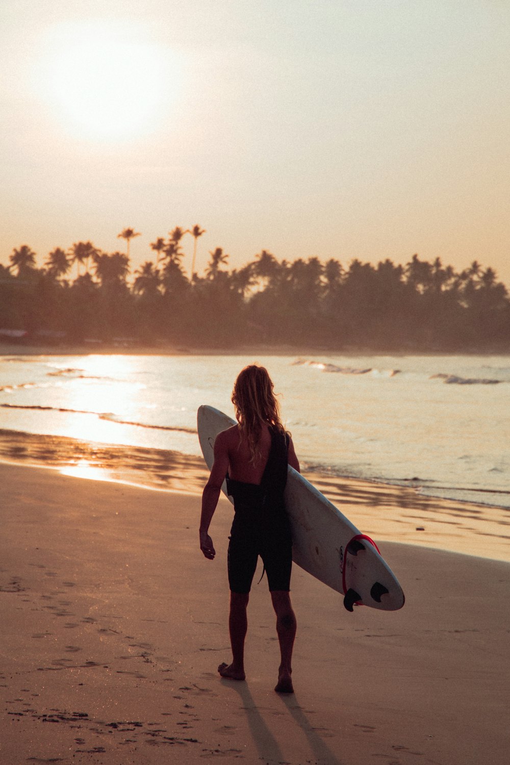 woman in black tank top holding white surfboard walking on beach during sunset