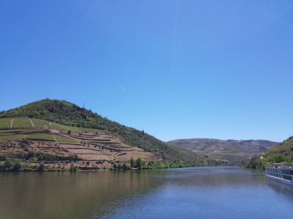 green and brown mountain beside body of water under blue sky during daytime
