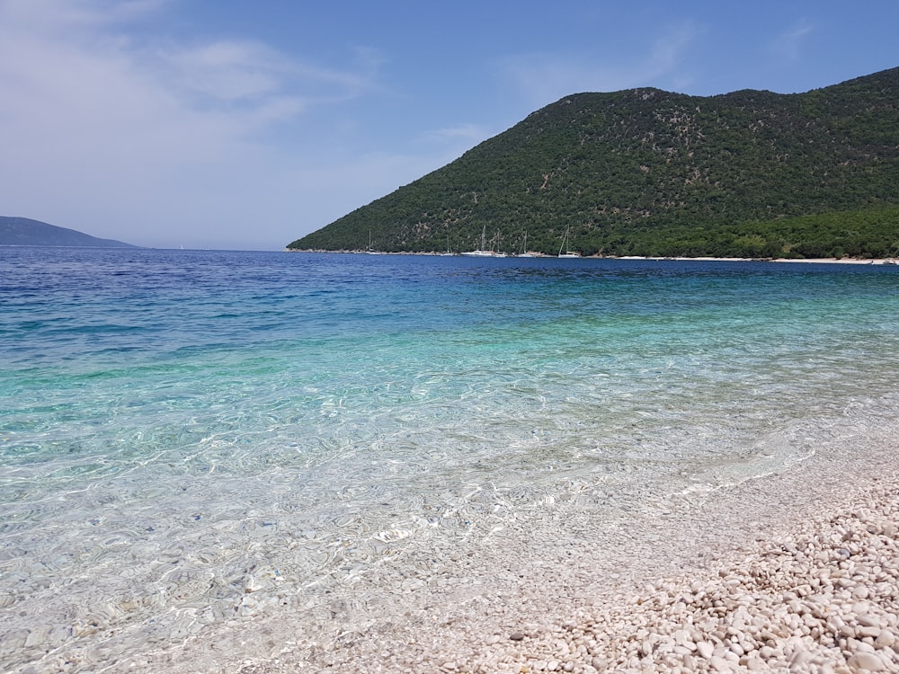 green mountain beside blue sea under blue sky during daytime