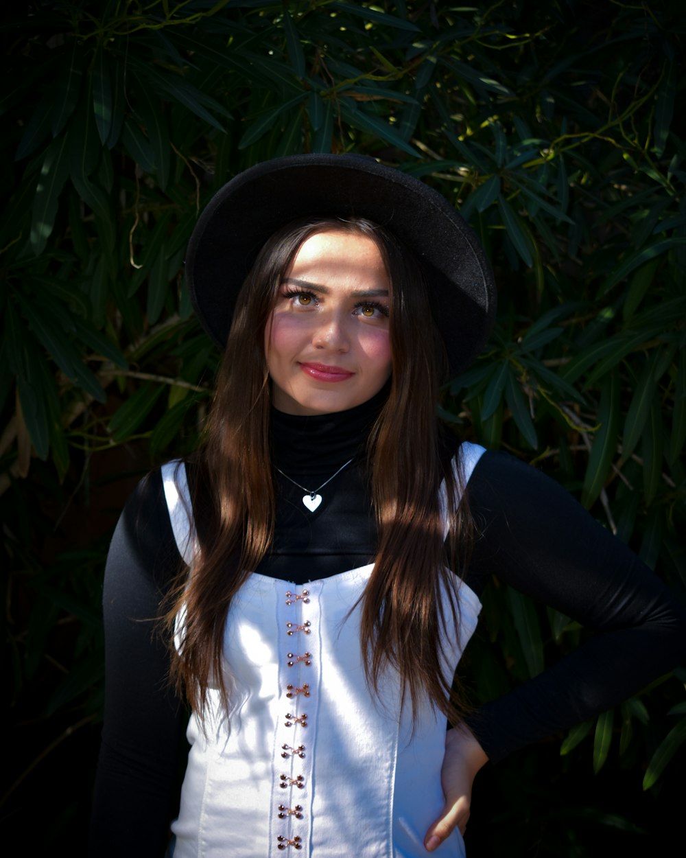 mulher na camisa de manga comprida preta e branca e chapéu preto em pé perto de plantas verdes