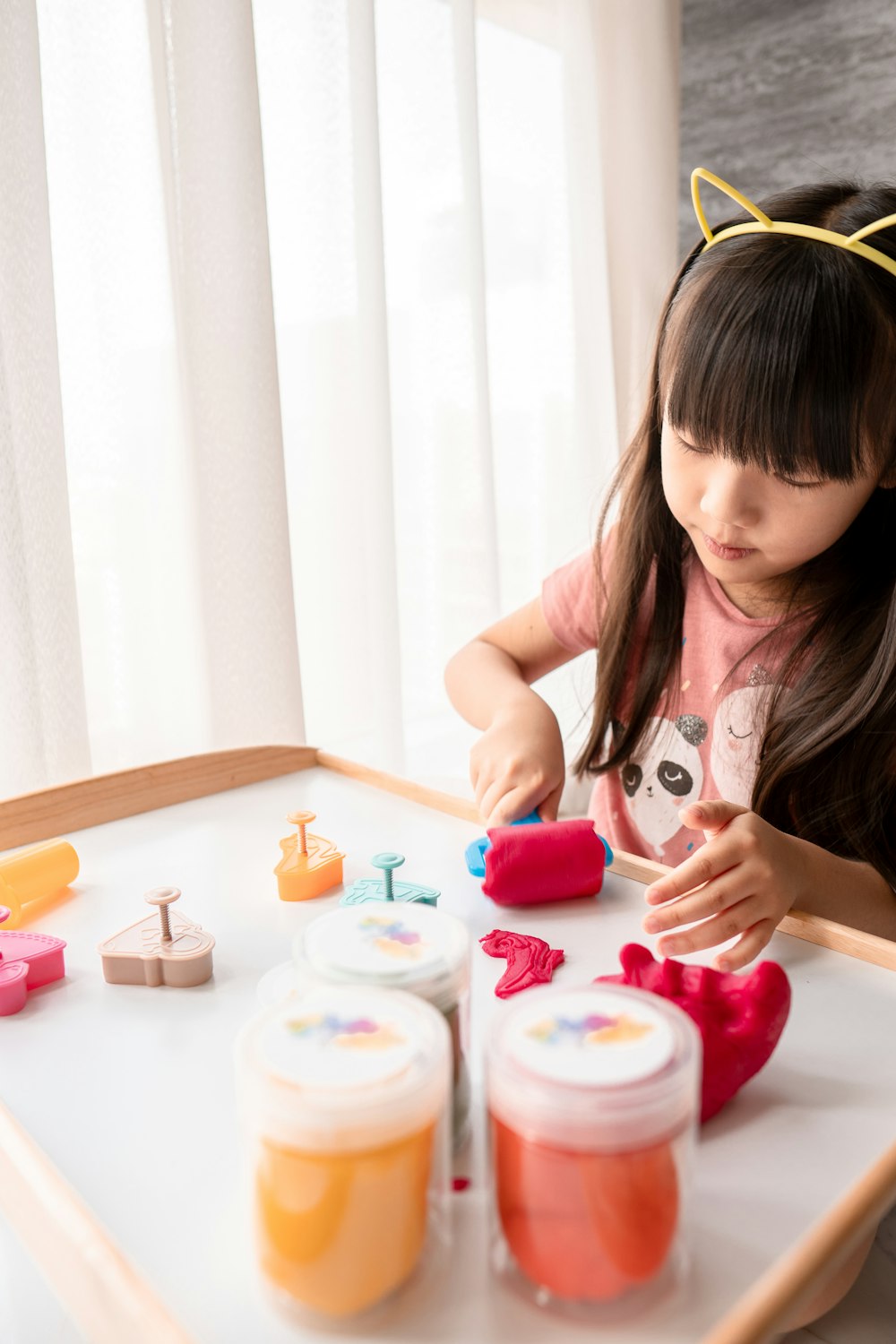 girl in white and pink tank top holding pink plastic toy