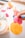 A playful scene featuring a hand pressing a pink mold onto a sheet of orange playdough, creating an imprint of a dress. Around the main activity, various colorful molds and containers are scattered, suggesting a creative, crafting session.