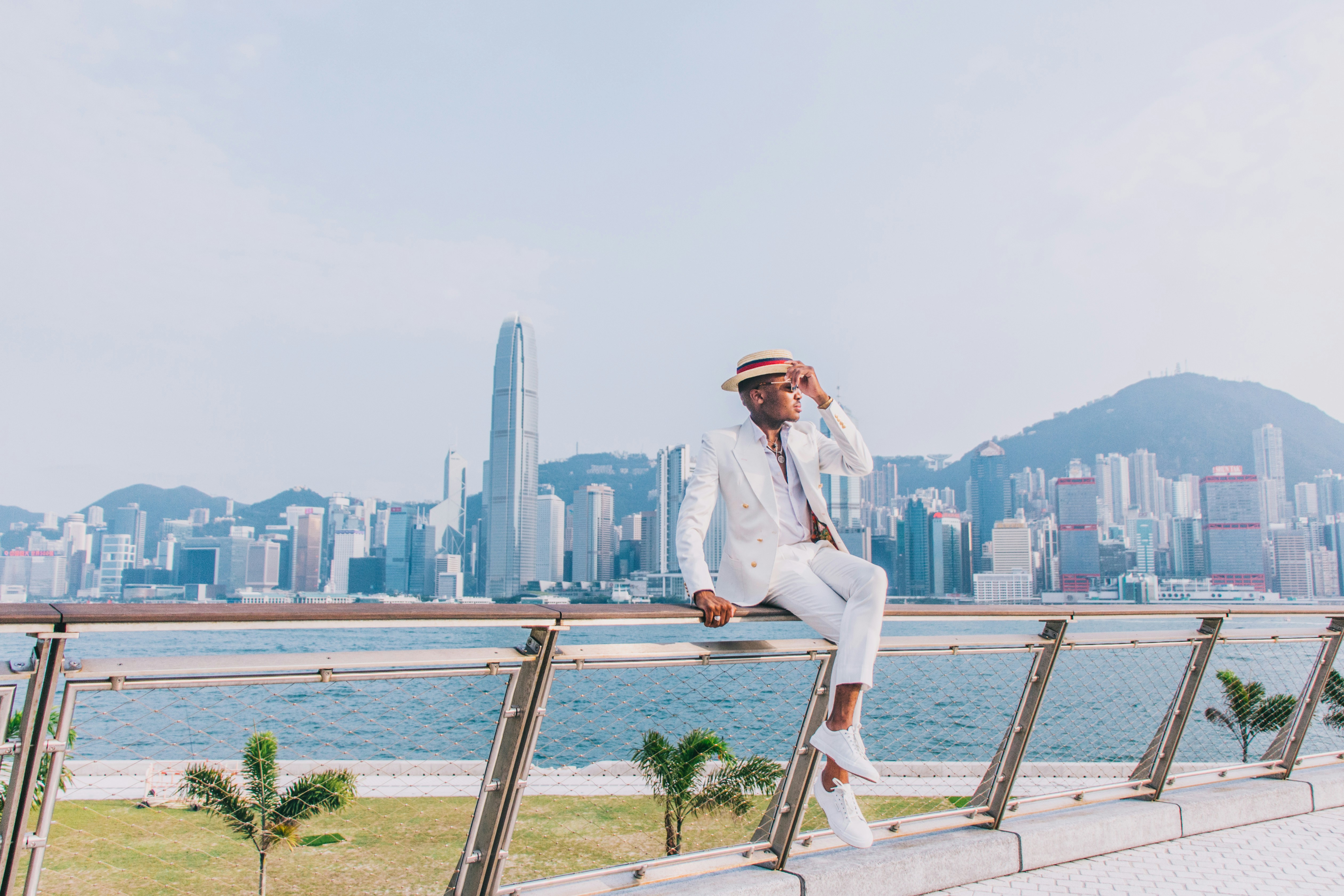 woman in white blazer and white pants sitting on brown wooden railings near body of water, 