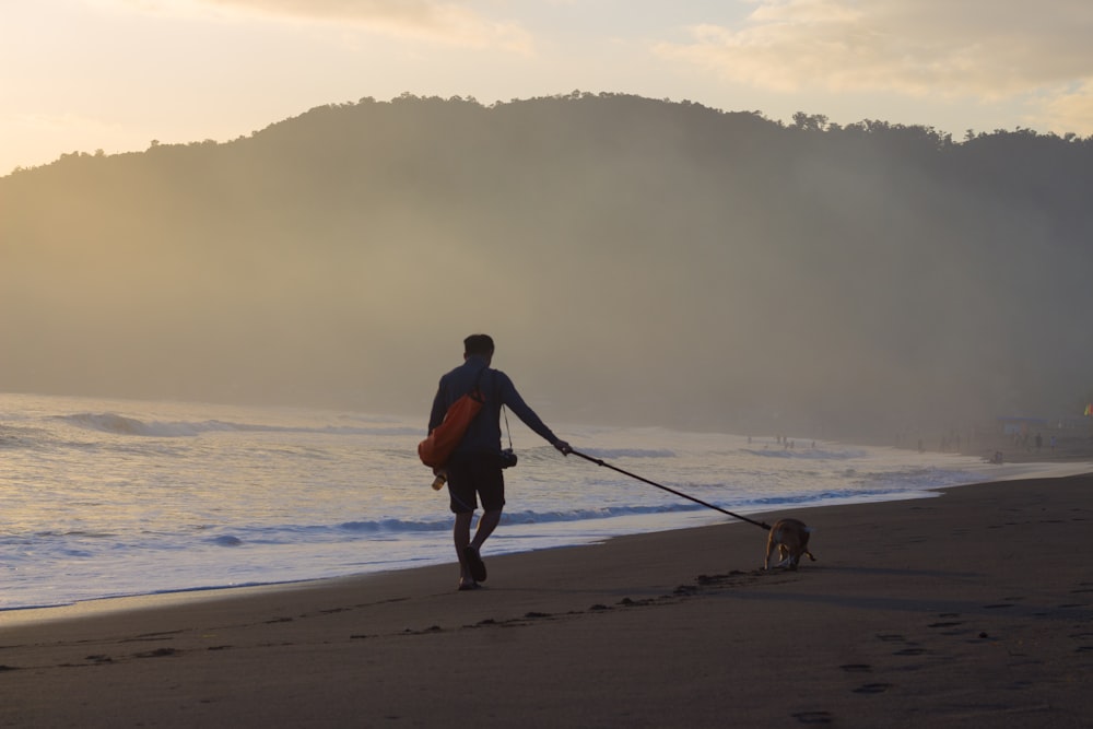 man in orange shirt and black shorts walking on beach during daytime