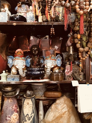 A cluttered assortment of decorative items including Asian figurines, ornate elephant statues, and beaded necklaces. There are vases with intricate designs, small boxes, and various objects made of stone and wood.