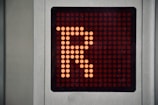 A digital display panel features a large orange letter 'R' made up of illuminated dots against a dark background. The panel is bordered by a metallic frame.