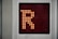 A digital display panel features a large orange letter 'R' made up of illuminated dots against a dark background. The panel is bordered by a metallic frame.