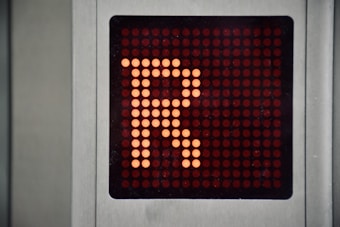 A digital display panel features a large orange letter 'R' made up of illuminated dots against a dark background. The panel is bordered by a metallic frame.