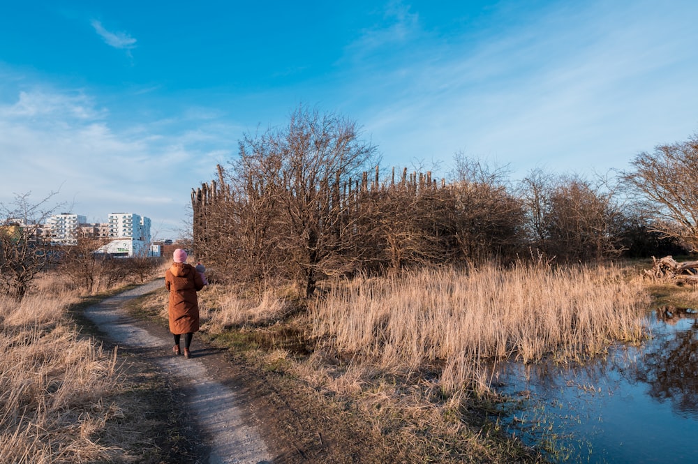woman in brown jacket walking on pathway beside river during daytime