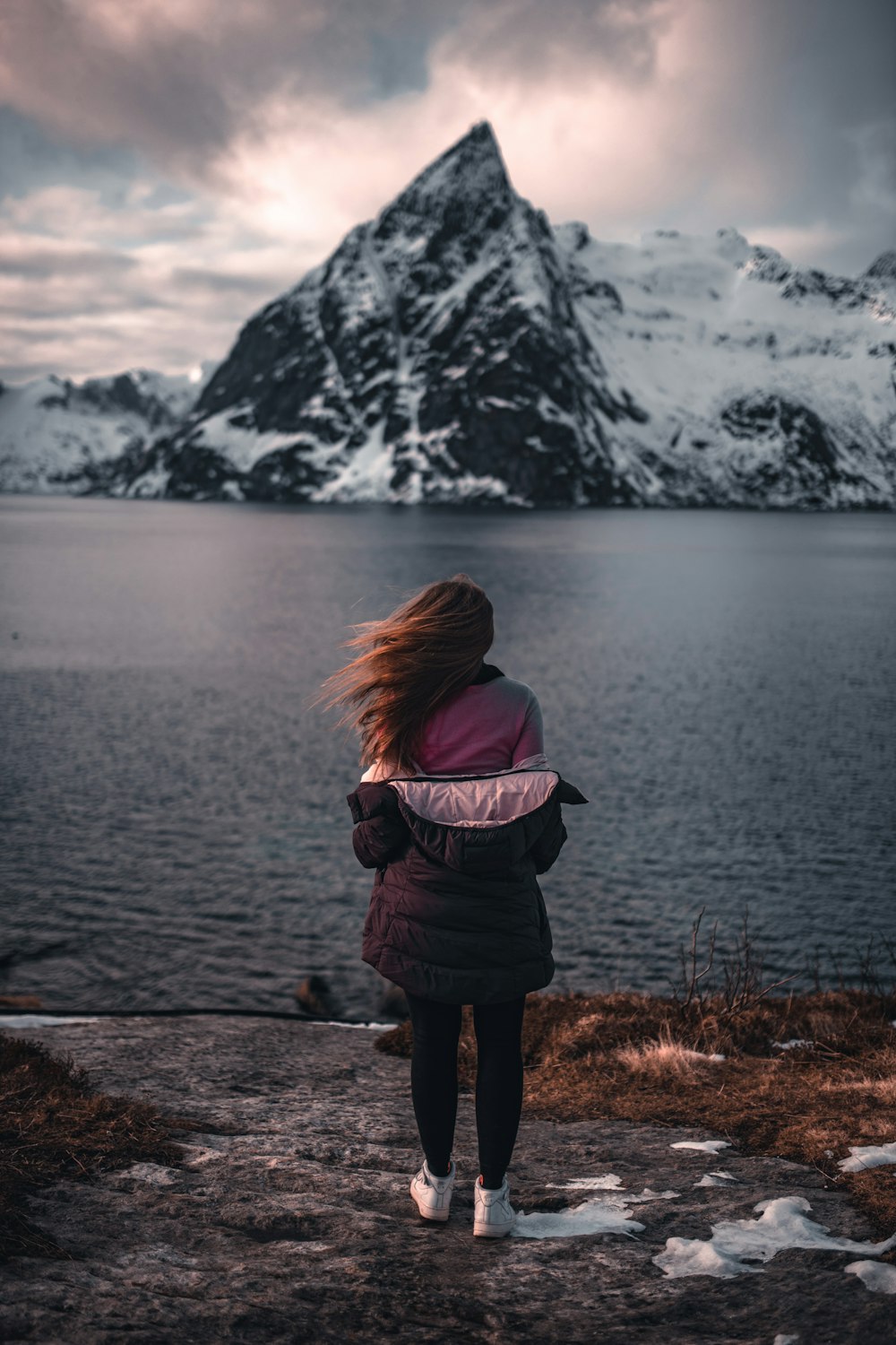 woman in purple jacket standing on brown grass field near body of water during daytime