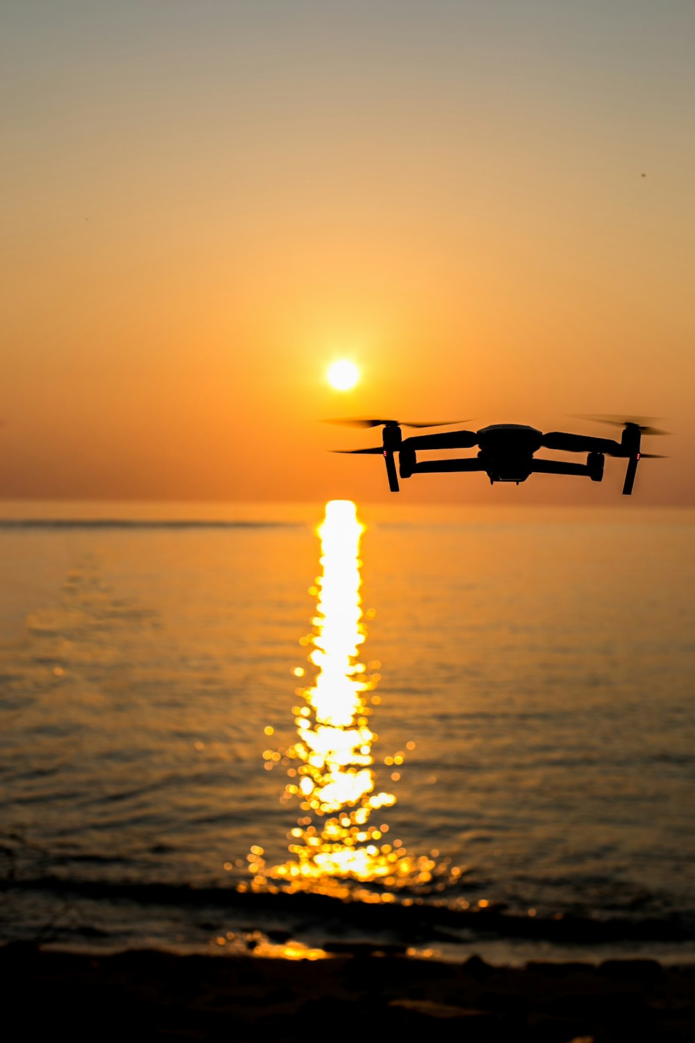 black drone flying over the sea during sunset