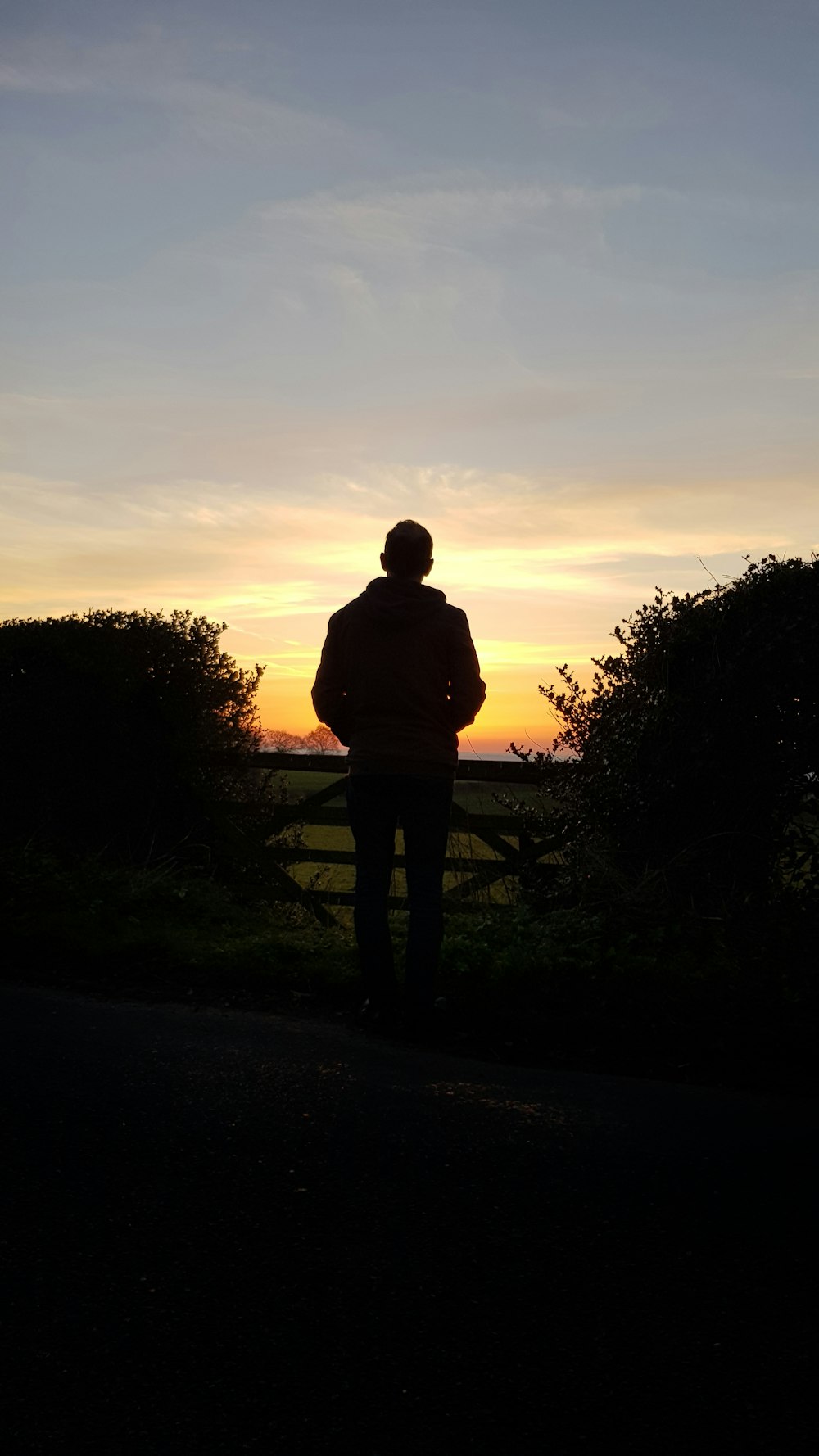 man in gray jacket standing on gray asphalt road during sunset