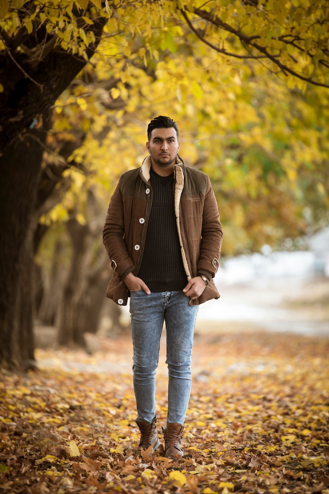 man in brown leather jacket and blue denim jeans standing on brown dirt road during daytime