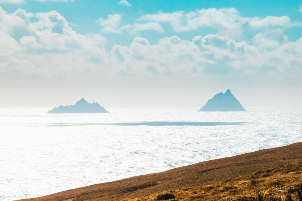 Brauner Berg in der Nähe von Gewässern unter weißen Wolken und blauem Himmel tagsüber