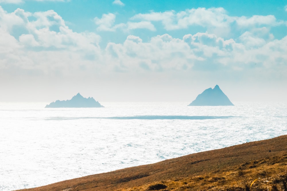 montanha marrom perto do corpo de água sob nuvens brancas e céu azul durante o dia