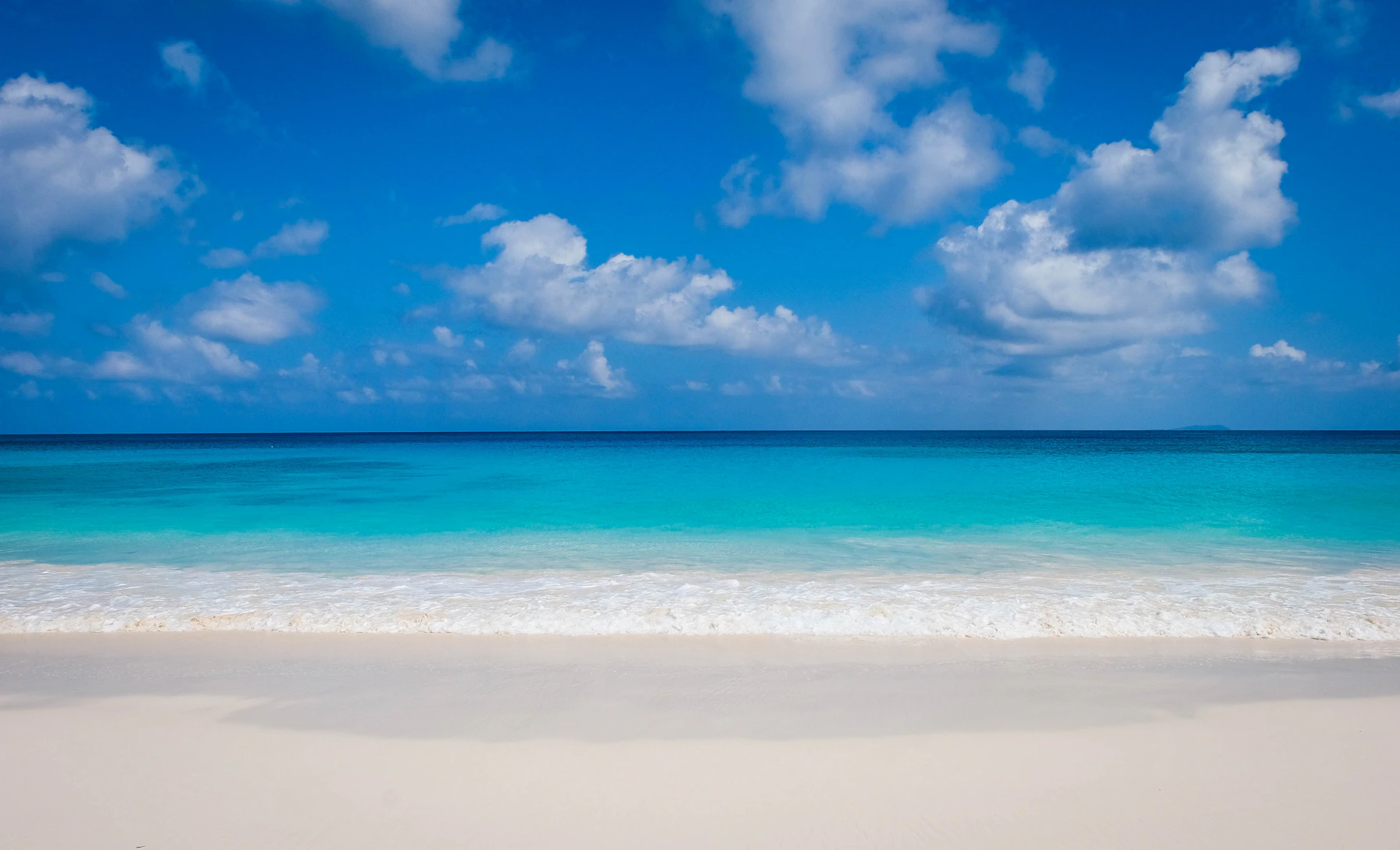 A serene beach with clear blue skies and gentle clouds framing the early morning sun.