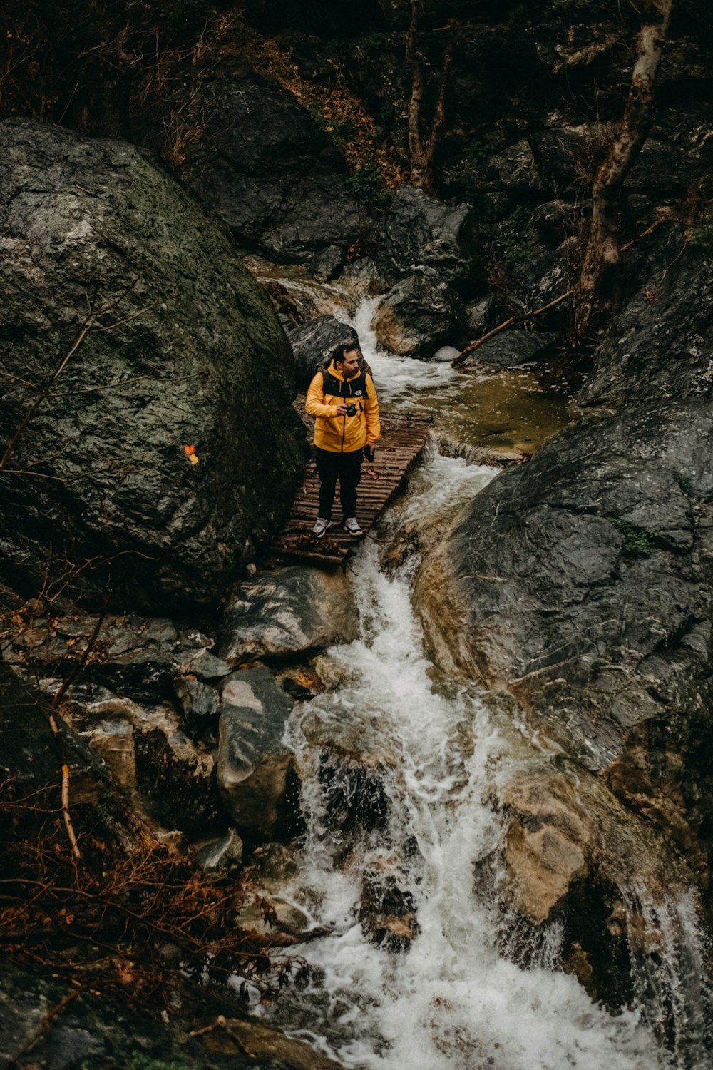 man in black and orange jacket standing on brown rock near river during daytime