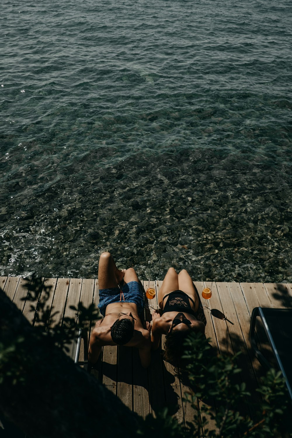 person in black flip flops sitting on wooden dock