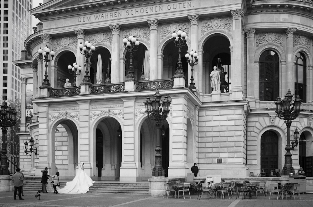 grayscale photo of people walking on sidewalk in front of building