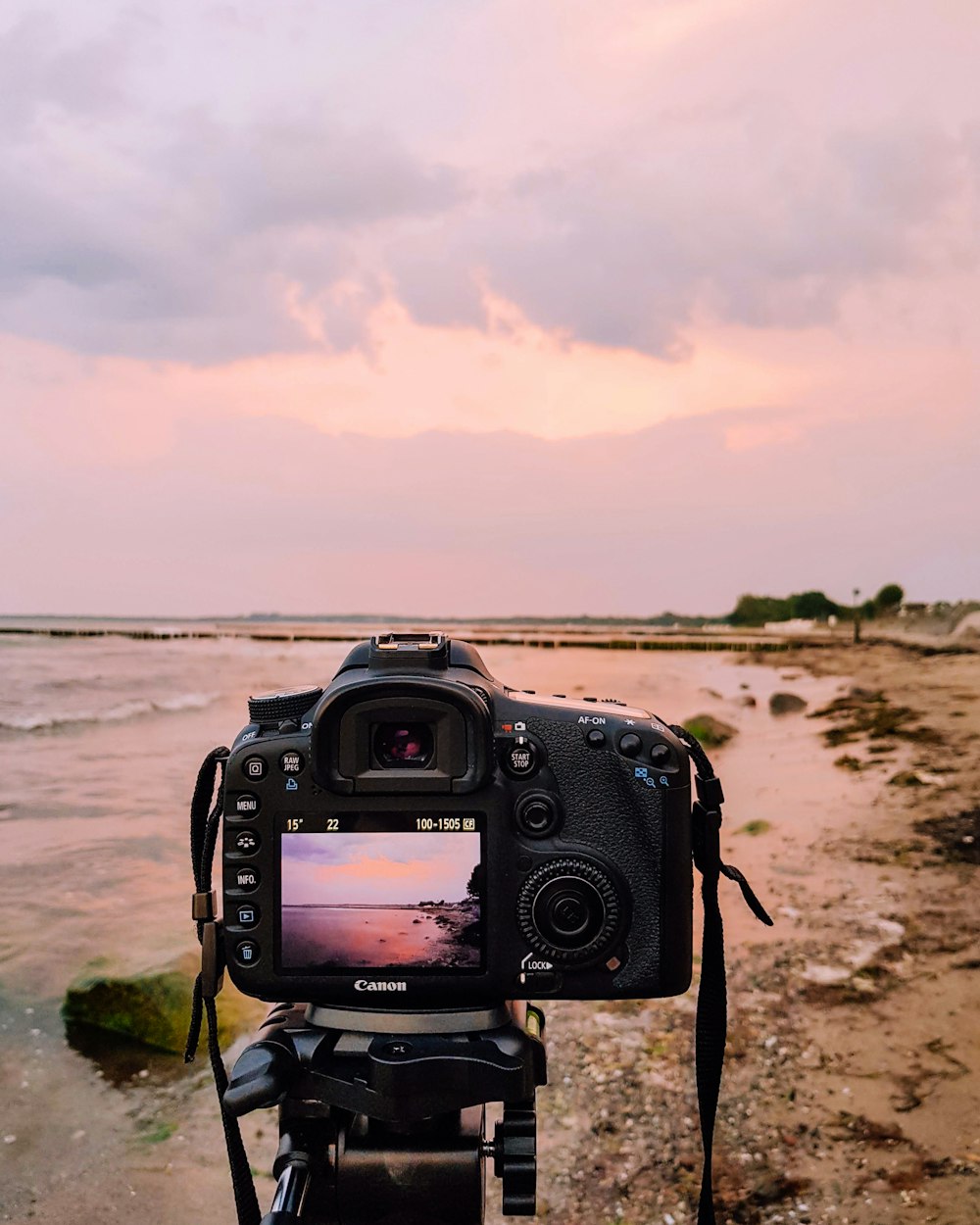 Appareil photo reflex numérique noir sur du sable brun près d’un plan d’eau pendant la journée