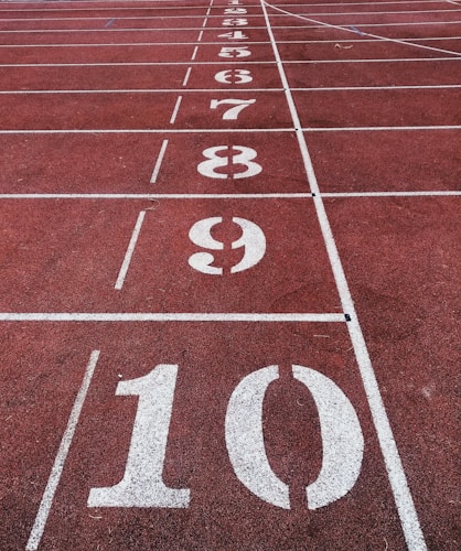 A running track with white lane markings and large numbers from 1 to 10 painted sequentially. The track surface is a reddish-brown color, typical of many athletic tracks.
