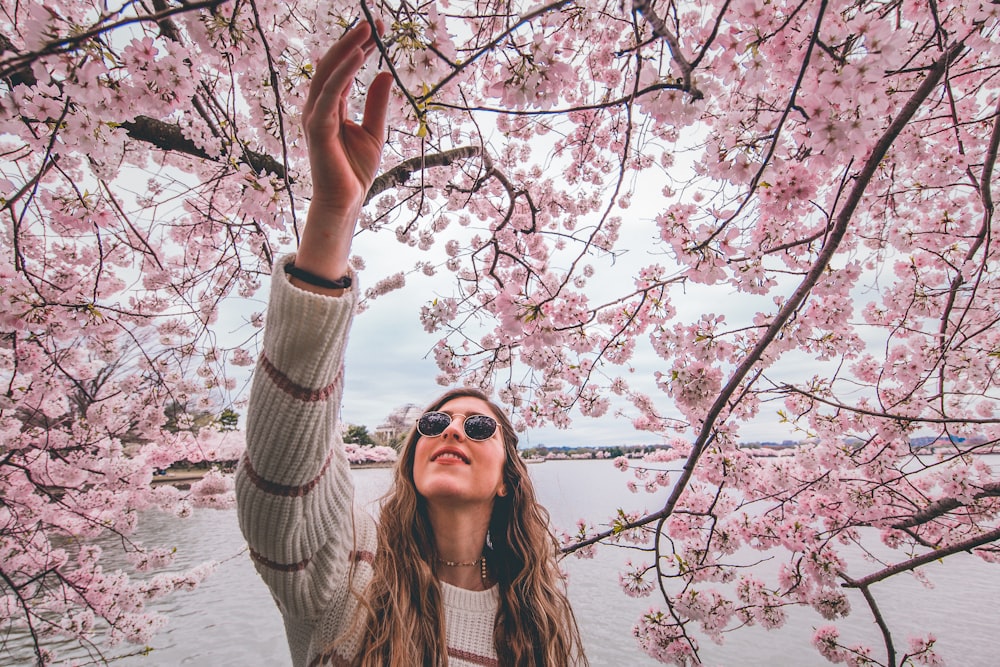 woman in white knit sweater standing near cherry blossom tree during daytime