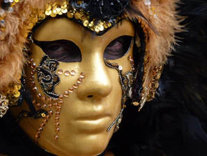 An elegant fashion mask with intricate gold filigree resting on a velvet black surface, glowing subtly in warm light.