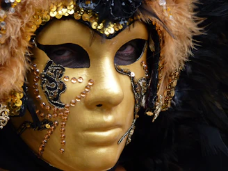 An elegant fashion mask with intricate gold filigree resting on a velvet black surface, glowing subtly in warm light.