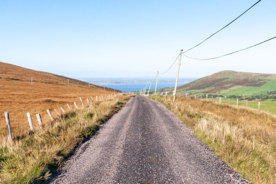 gray asphalt road between brown grass field under blue sky during daytime in County Kerry Ireland