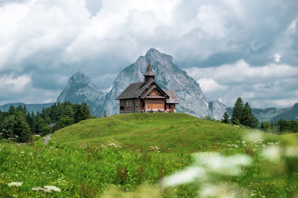 brown wooden house on green grass field near mountain under white clouds during daytime