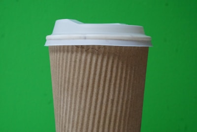 A disposable coffee cup with a textured brown sleeve and white plastic lid is set against a vibrant green background.