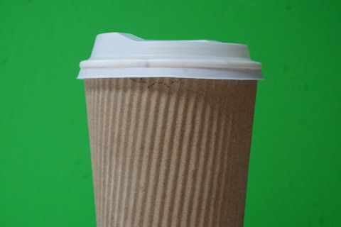 A disposable coffee cup with a textured brown sleeve and white plastic lid is set against a vibrant green background.