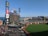 A baseball stadium with a large screen displaying a logo in the center. The stands are partially filled with spectators, and there are various advertisements surrounding the screen. The view includes a green field, with buildings and water visible in the background, suggesting the stadium is near a waterfront city area.