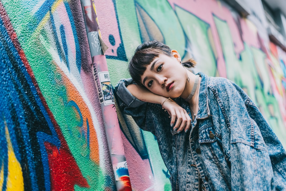 girl in blue denim jacket standing beside graffiti wall during daytime