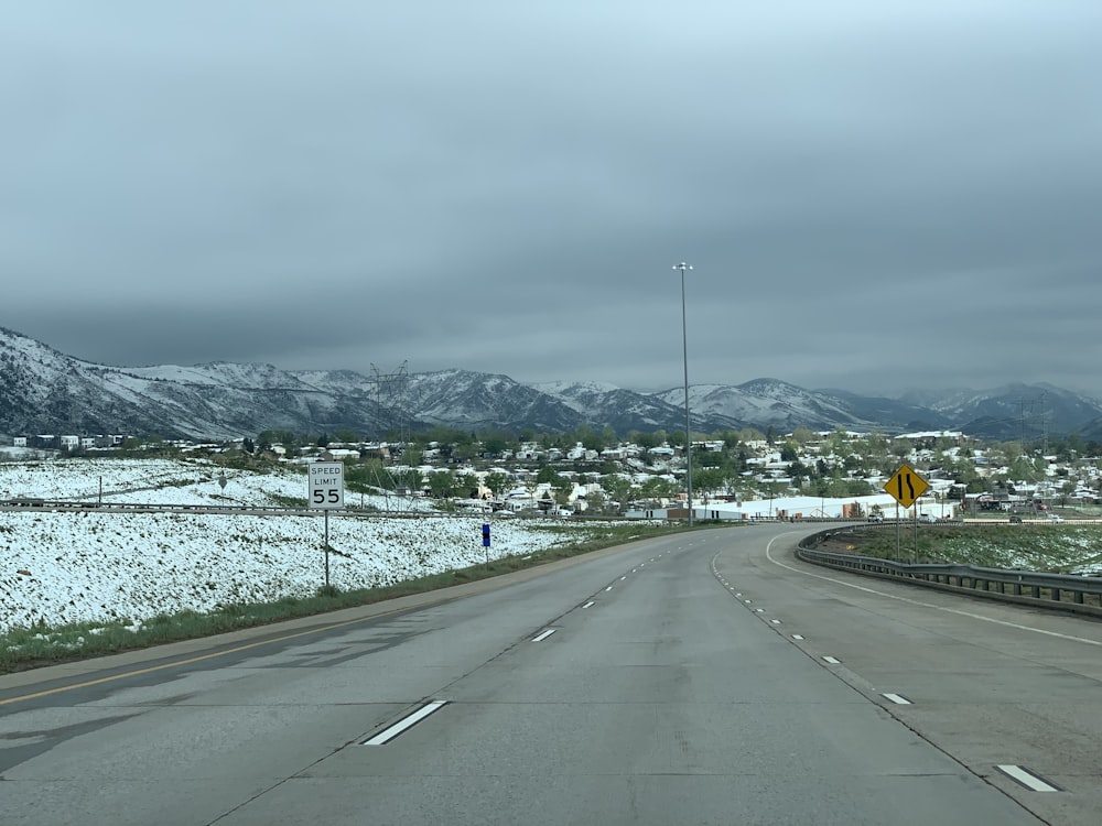 gray concrete road near green trees and mountain during daytime