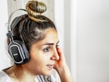A person with a bun hairstyle wearing large black headphones appears to be listening attentively. The background is neutral and well-lit.